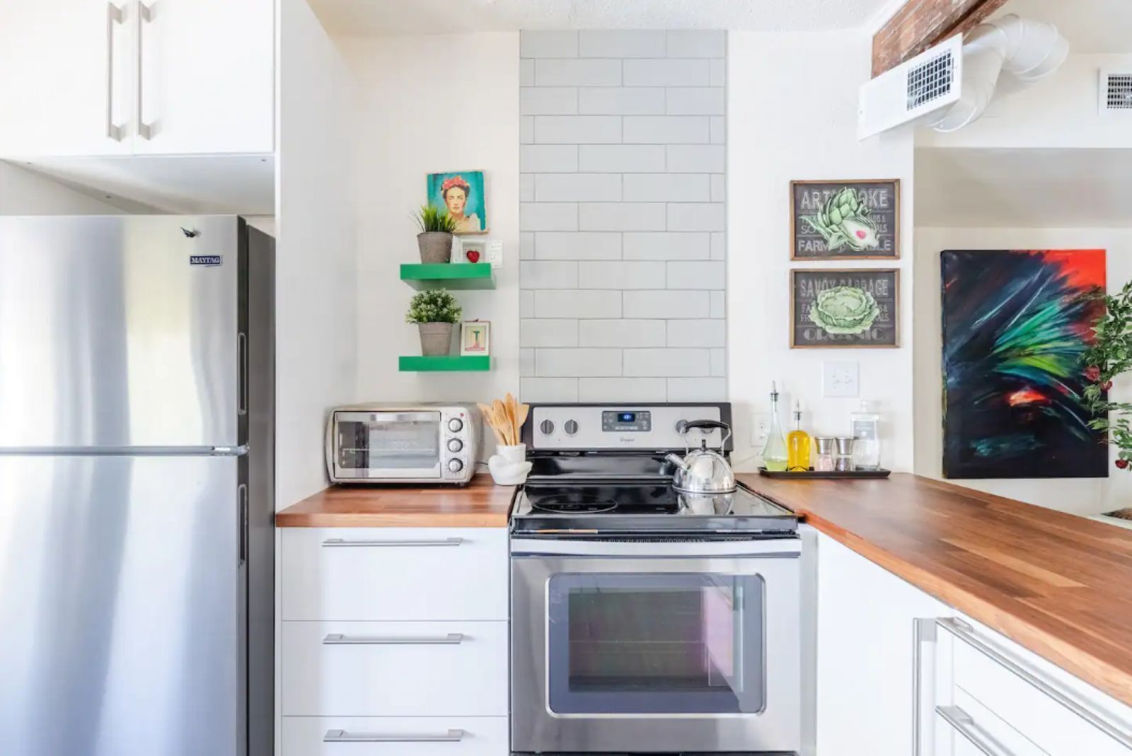 A modern kitchen with a stainless steel refrigerator, a built-in oven, and a microwave. There are wooden cabinets and a countertop with a toaster and a kettle.