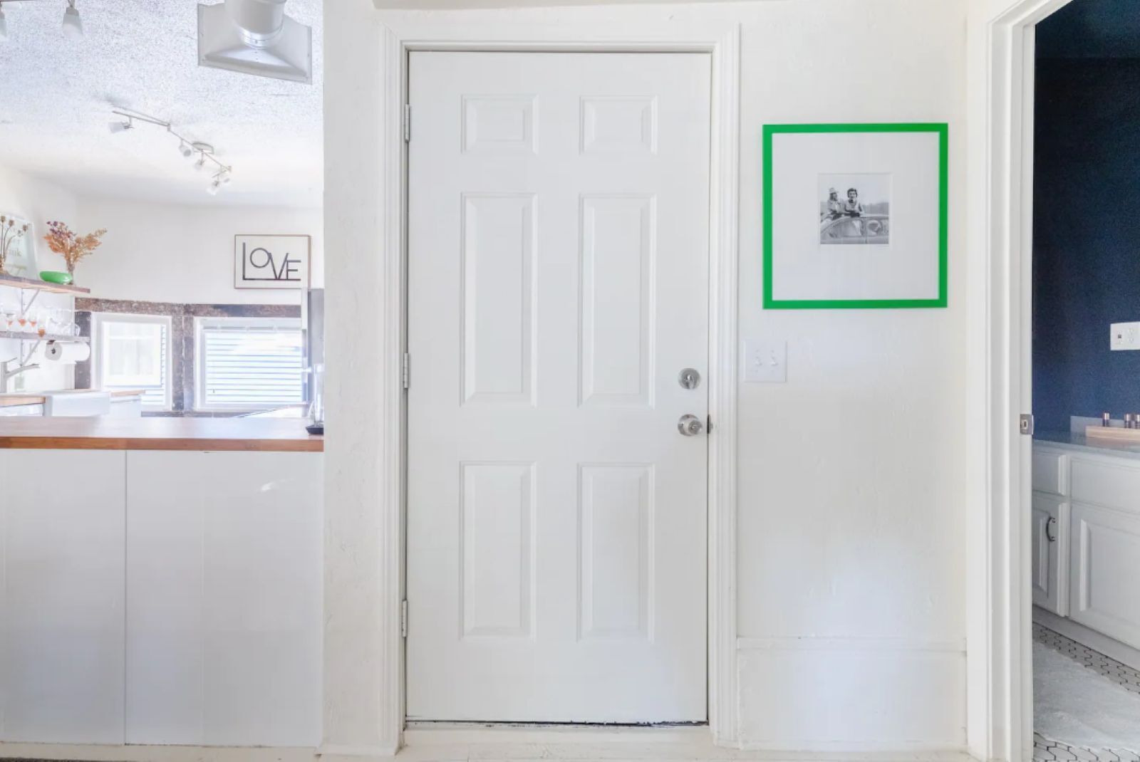 Una puerta blanca con un cuadro enmarcado en la pared a la derecha.