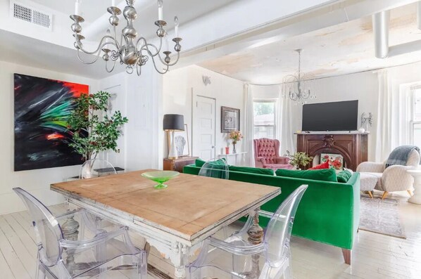 Ein geräumiges Wohnzimmer mit einem Holzessttisch, klaren Stühlen, einem grünen Sofa und einem Fernseher auf einem Holzboden.