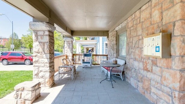 A covered outdoor area with stone pillars, wicker furniture, and a stone wall.