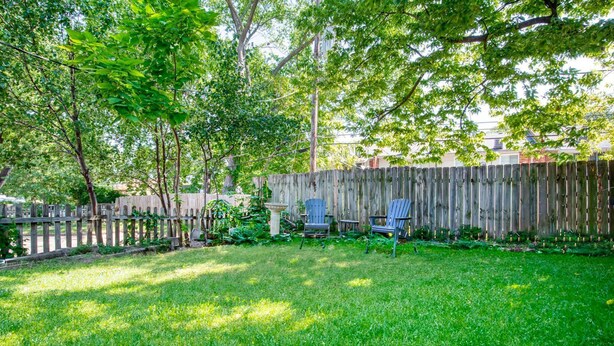 A backyard with a wooden fence, two Adirondack chairs, and a birdbath.
