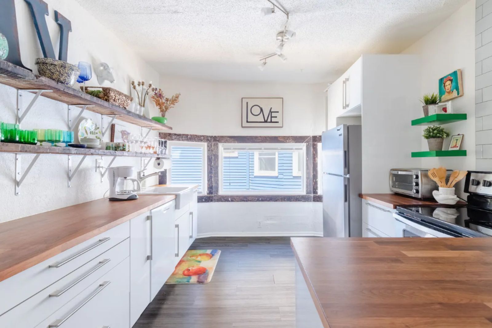 A modern kitchen with white cabinets, a wooden countertop, and a 'LOVE' sign on the wall.