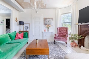 Ein Wohnzimmer mit einem grünen Sofa, einem Holztisch, einem pinken Sessel und einem Kamin.