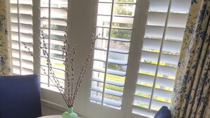 A room with a round table, two blue chairs, a vase with branches, and a window with white shutters. - Charming suite with private entrance (Dallas)