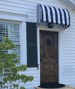Uma casa com porta de madeira, janela com persianas e toldo listrado em preto e branco.