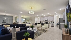 A modern living room with a dark sofa, a coffee table, and a chandelier. - NEW Lake View Villa Near Disney w/ Pool & Spa! (Four Corners)
