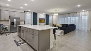 A modern kitchen with a central island, a dining area with a chair, and a living room with a sofa. - NEW Lake View Villa Near Disney w/ Pool & Spa! (Four Corners)