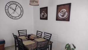 Ein Essbereich mit einem runden Tisch, vier Stühlen, einer Uhr und zwei gerahmten Kaffeetassen-Kunstwerken.
