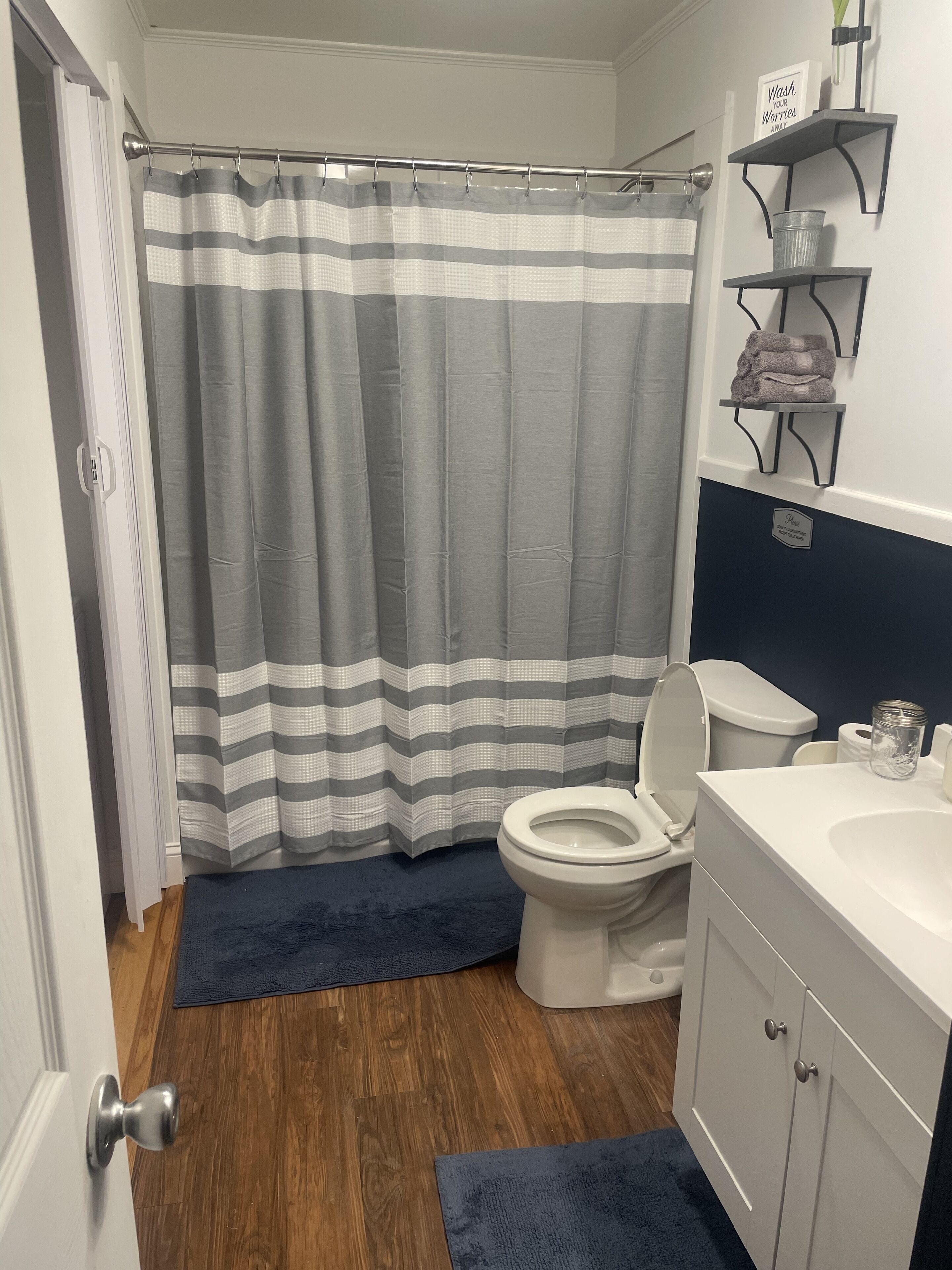 Ein Badezimmer mit gestreifter Duschvorhang, Toilette, Waschbecken und einer kleinen Ablage mit Handtüchern.