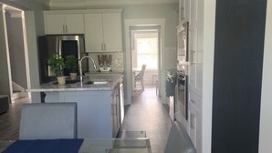 Una cucina moderna con mobili bianchi, elettrodomestici in acciaio inossidabile e un'area pranzo con tavolo in vetro e sottopiatti blu.