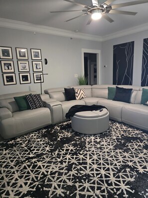 A living room with a sectional sofa, a round ottoman, and a patterned rug.