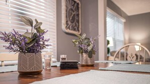 Ein Essbereich mit einem Holztisch, zwei topfgepflanzten Pflanzen mit violetten Blüten, einem Bücherstapel und einer Wanddekoration.