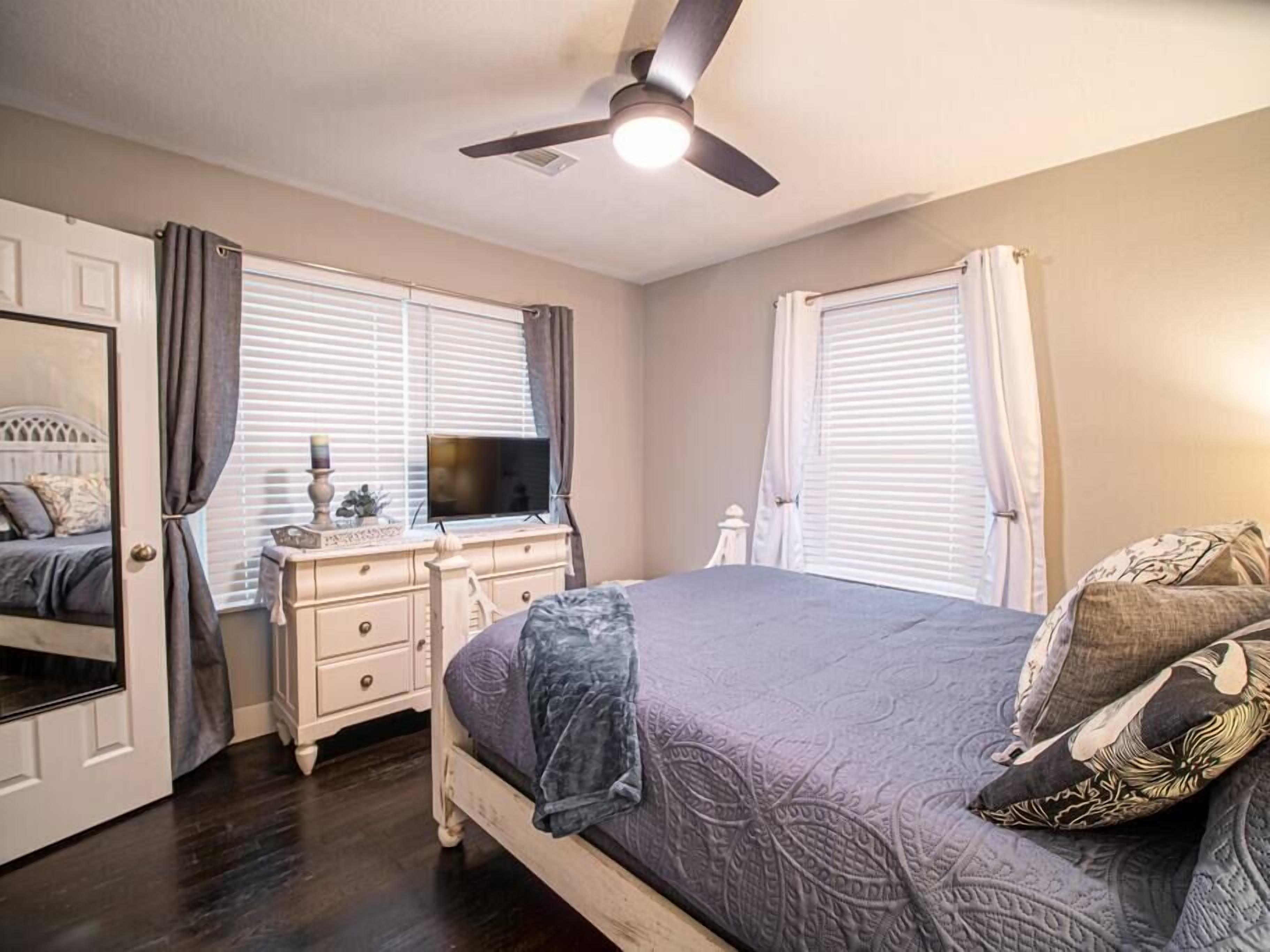 A bedroom with a bed, dresser, TV, and ceiling fan.