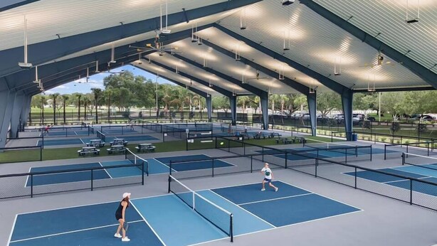 Ein Tennisplatz mit mehreren Spielfeldern, einem überdachten Sitzbereich und Blick auf den umliegenden Park.
