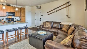 A modern living room with a leather sofa, a coffee table, and a kitchen area with wooden cabinets and a microwave.