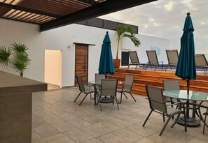 An outdoor seating area with tables and chairs, umbrellas, and a wooden staircase leading to a higher level. - Lovely Modern Condo 5 Blks From the Beach! (Playa del Carmen)