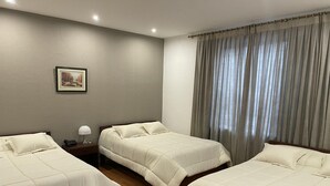 A hotel room with two beds, a nightstand with a lamp, a framed picture on the wall, and a window with curtains. - ALSTON INN HOTEL (Quito)