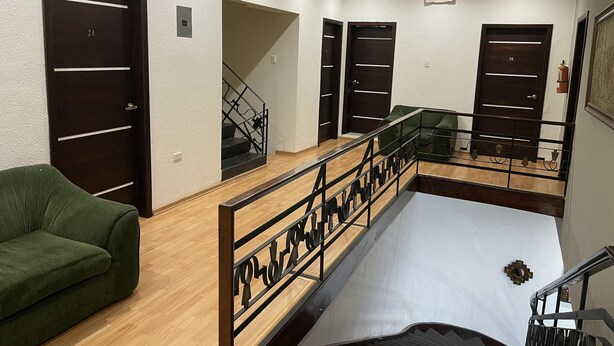 A hotel room with a wooden floor, a green sofa, a staircase with a metal railing, and multiple dark wooden doors. - ALSTON INN HOTEL (Quito)