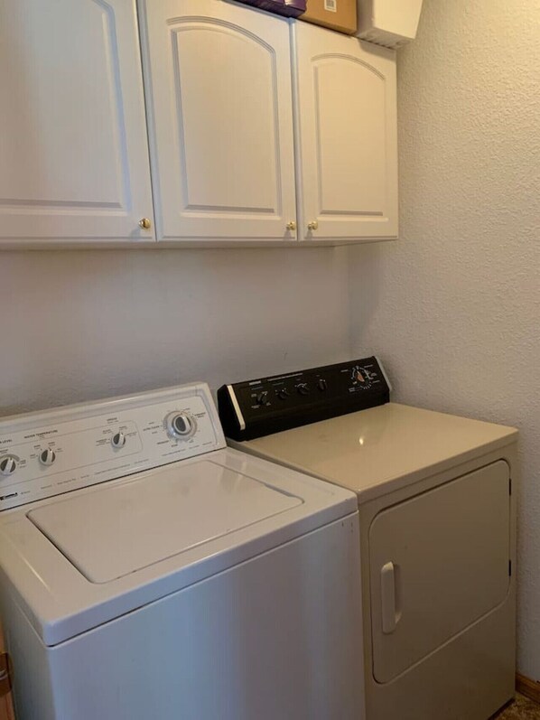 A laundry area with a front-loading washer and dryer, white cabinetry above, and a small shelf with a box.