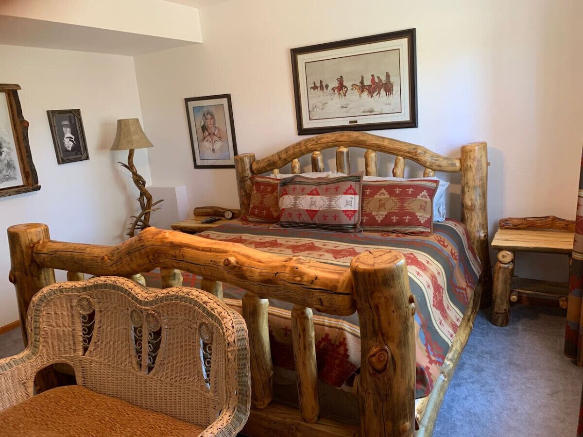 A rustic bedroom with a wooden bed frame, a woven chair, and a small bedside table.