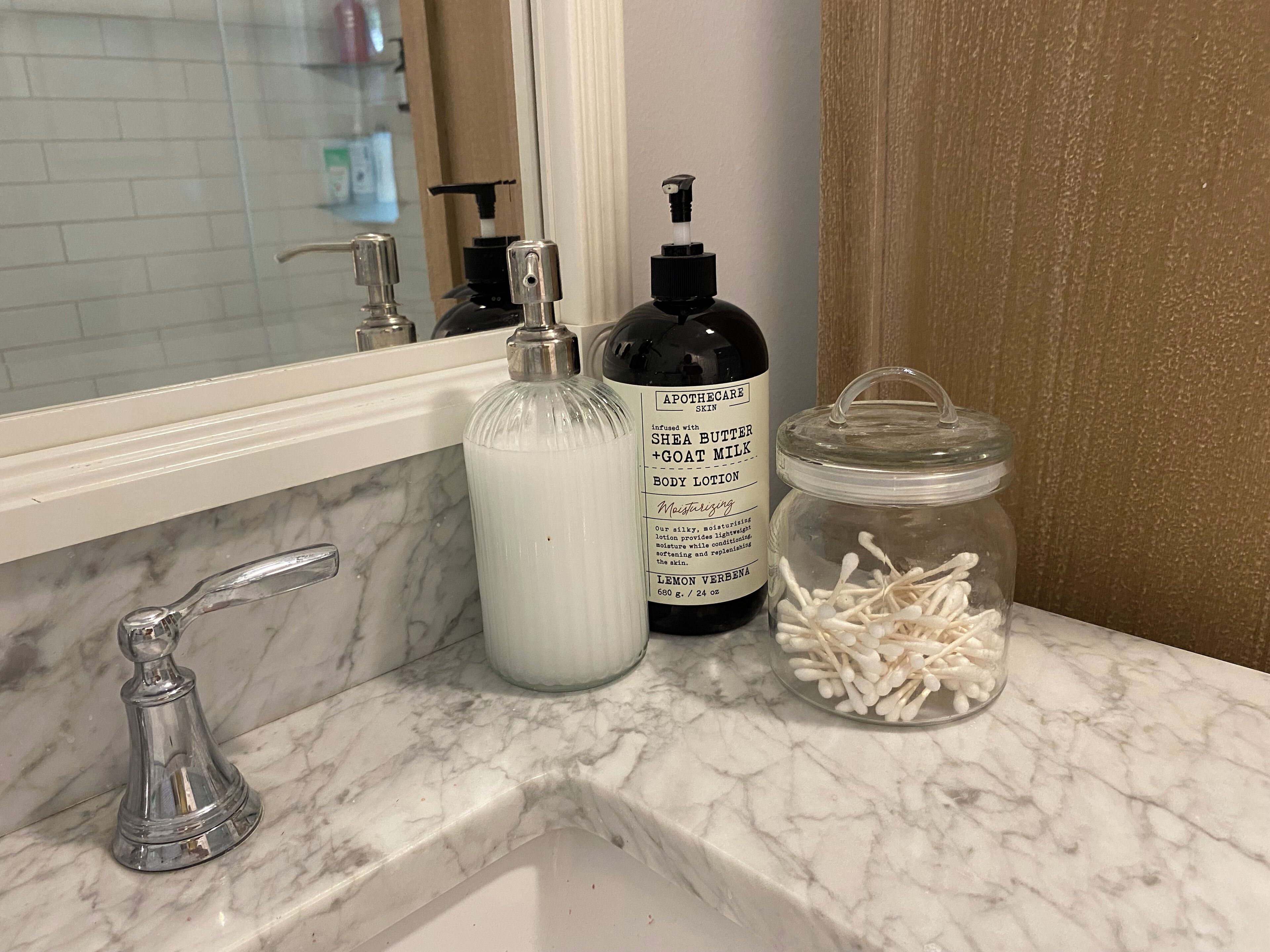 Un lavabo de salle de bain avec un plan de toilette en marbre, un flacon de lotion, un pot de cotons-tiges et un miroir.