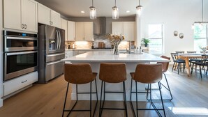 A modern kitchen with stainless steel appliances, a central island with bar stools, and pendant lighting.