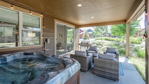 A covered outdoor area with a hot tub, wicker furniture, and a grill.