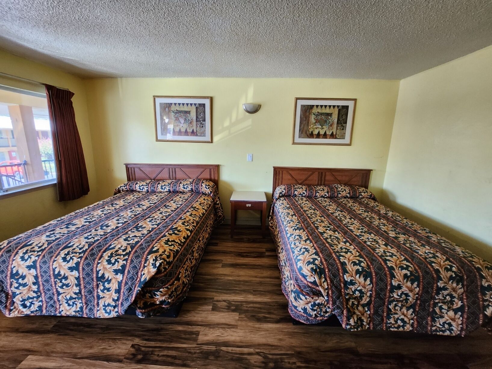 A room with two beds, wooden flooring, and two framed pictures on the wall.