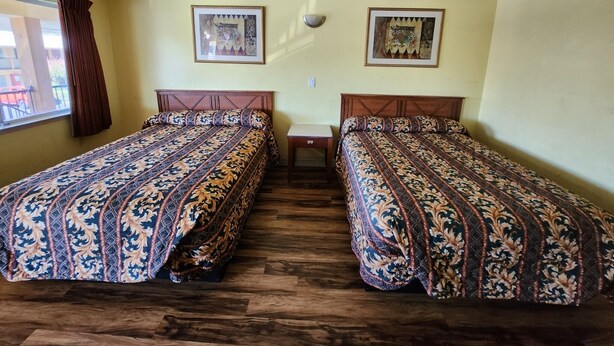 A room with two beds, wooden flooring, and two framed pictures on the wall. - Vince's Motel Inc. (Sacramento)