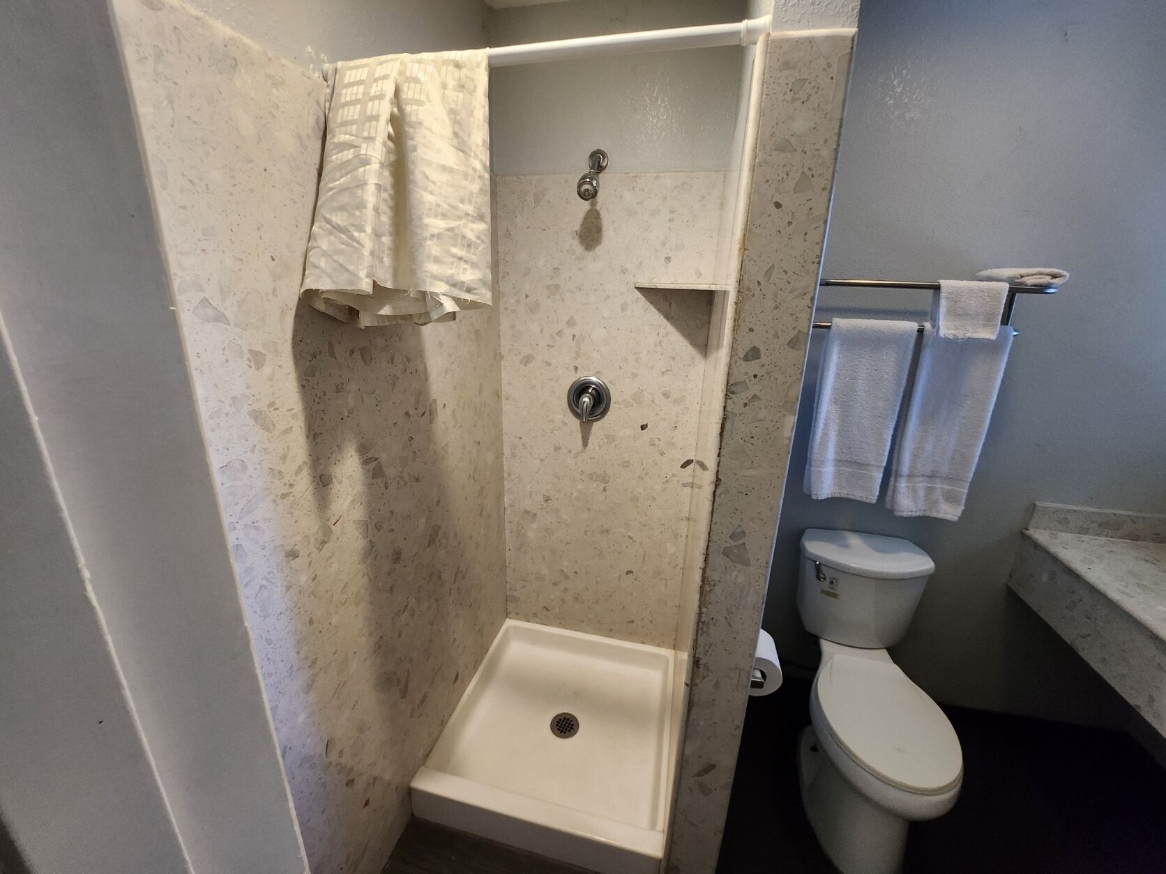 A small, tiled bathroom with a shower, toilet, and a towel rack.