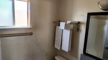 Een kleine badkamer met toilet, wastafel en spiegel. Boven het toilet is een raam en er hangt een handdoekrek met twee handdoeken.