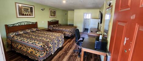 A hotel room with two beds, a desk, a chair, a TV, and a door.