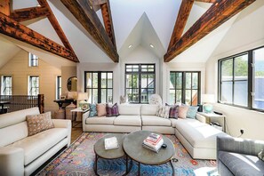 A spacious living room with a large sectional sofa, two coffee tables, and a view of the outdoors through large windows.