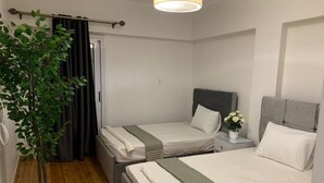 Una habitació d'hotel amb dos llits individuals, una planta en test, una taula de nit amb un ram de flors i una barra de cortina.