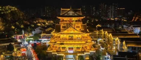 Un bâtiment traditionnel à plusieurs étages, avec des fenêtres illuminées et une rue adjacente, le tout baigné par la lumière de la nuit.