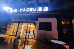 A hotel entrance with a glass facade, a signboard, and a small outdoor seating area. - Mengfei Hotel (Liuzhou Yaobu Old Town) (Liuzhou)