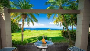 Een overdekt terras met een tafel, twee stoelen en uitzicht op de oceaan.