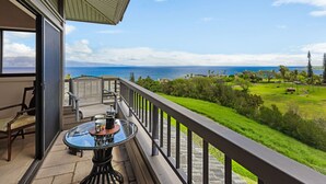 Un balcone con un tavolo in vetro, sedie e vista sull'oceano e sul campo da golf.