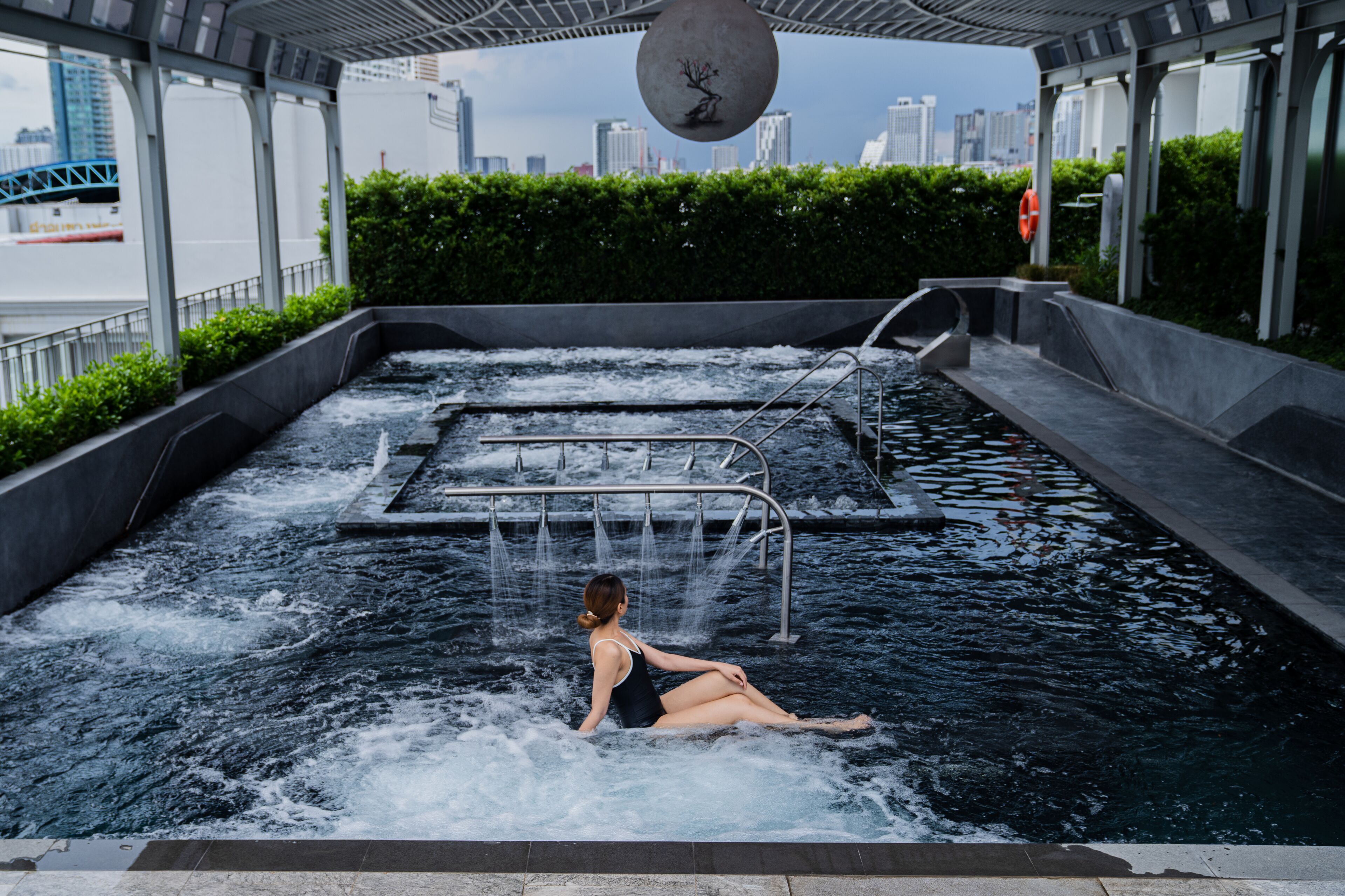A woman sitting in a water feature with a cityscape in the background.