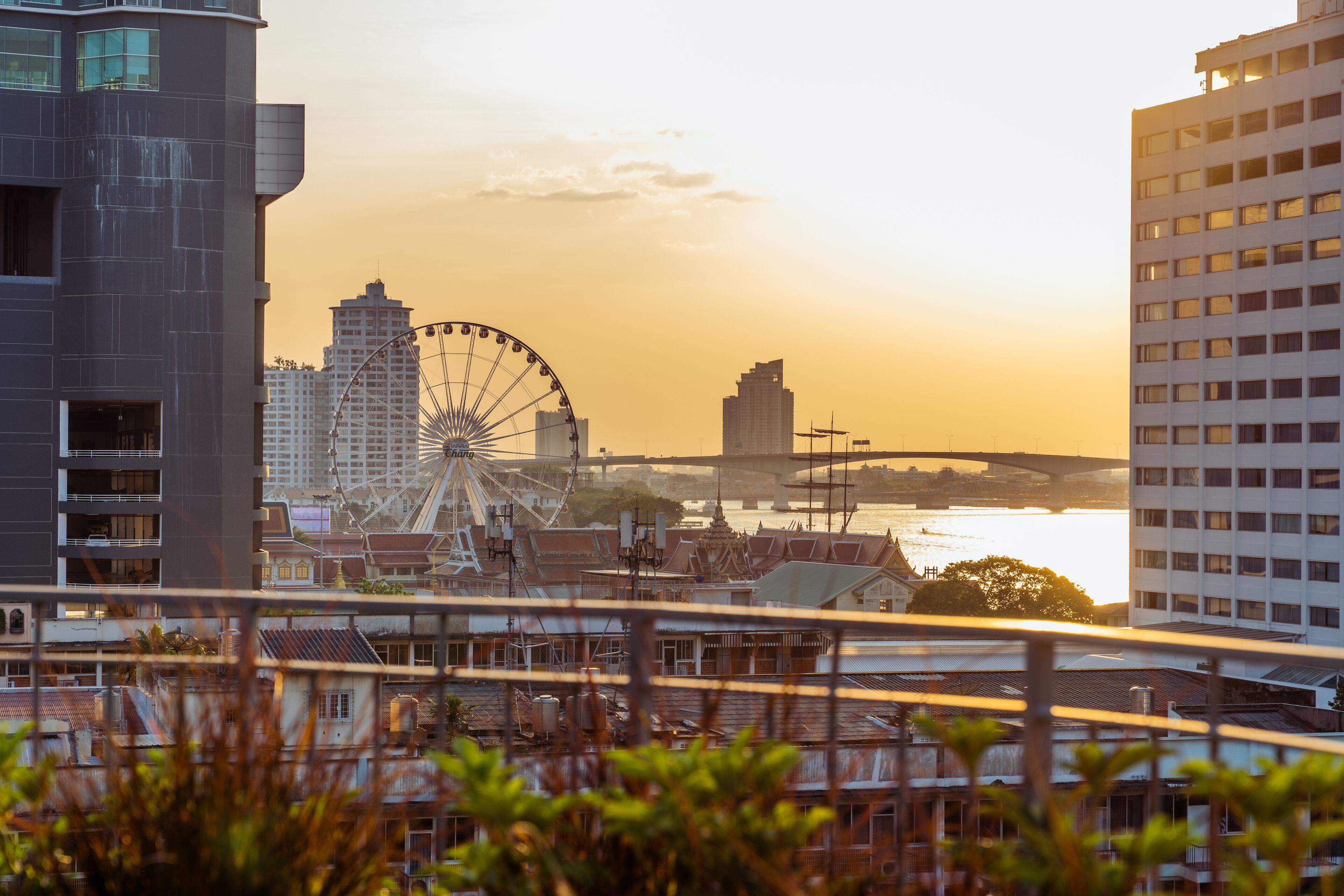 A cityscape with a Ferris wheel, modern buildings, and a river.