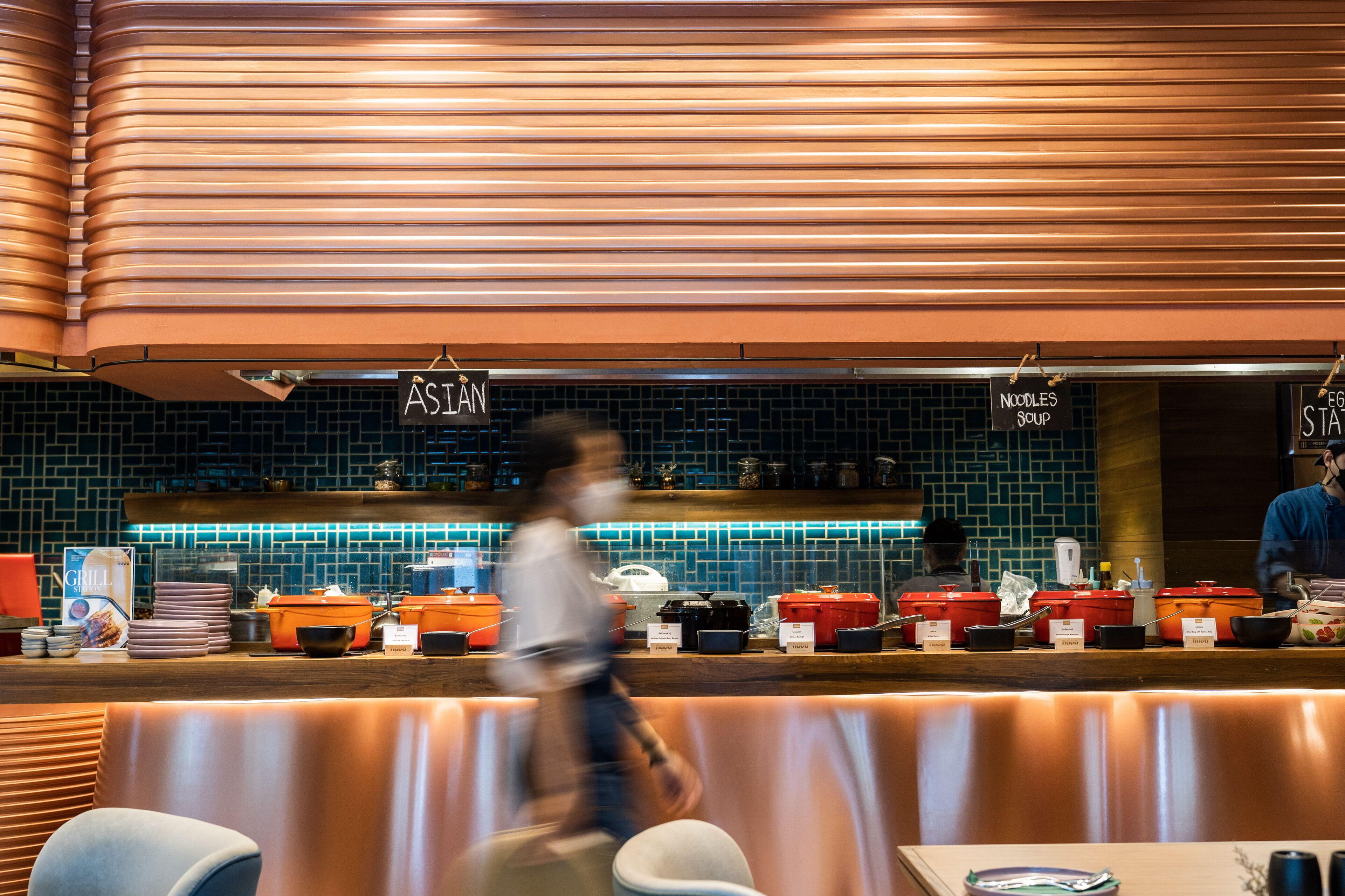 Un restaurante con decoración moderna, que cuenta con una barra con recipientes etiquetados y un letrero que indica la zona de sopa de fideos.