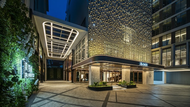 A modern hotel entrance with a glass facade, a well-lit entrance, and a landscaped area with planters. - The Salil Hotel Riverside Bangkok (Bangkok)