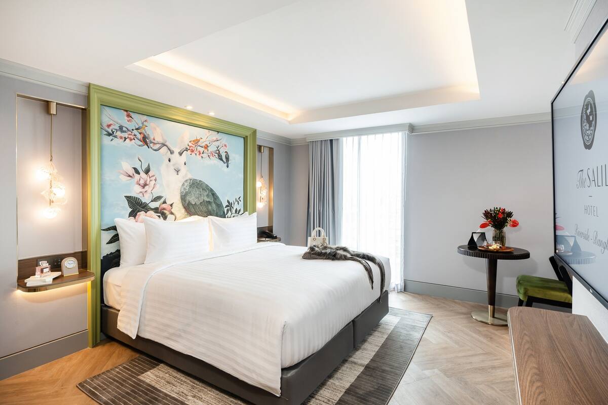 Een moderne hotelkamer met een groot bed, een schilderij aan de muur, een klein tafeltje met een bloevas en een televisie aan de wand.