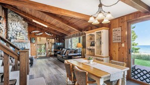 L’intérieur d’un chalet rustique, avec un mur en pierre, des poutres en bois, un coin repas et une vue sur le lac.