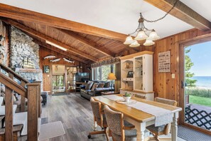 L’intérieur d’un chalet rustique, avec un mur en pierre, des poutres en bois, un coin repas et une vue sur le lac.