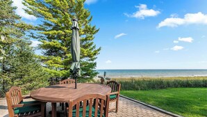Une table extérieure en bois, avec des chaises, un parasol vert et une vue sur la plage.