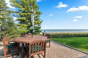 A wooden outdoor table with chairs, a green umbrella, and a view of the beach.