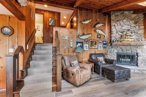 A wooden interior with a stone fireplace, a staircase, leather furniture, and fish decorations.