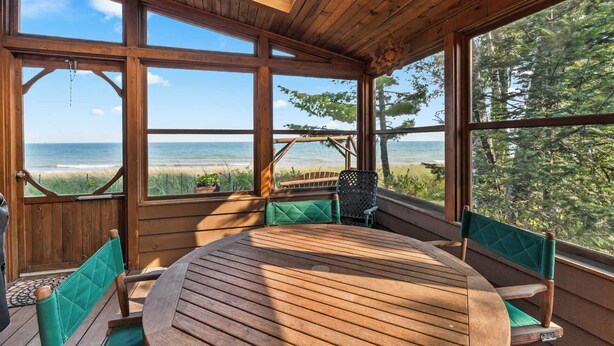 Une terrasse en bois avec une table ronde et des chaises vertes à coussins, donnant sur une plage et l’océan.