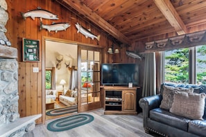 L’intérieur chaleureux d’un chalet avec un plafond en bois, un téléviseur, un canapé en cuir et des têtes d’animaux empaillées, notamment des poissons et des cerfs, accrochées aux murs.